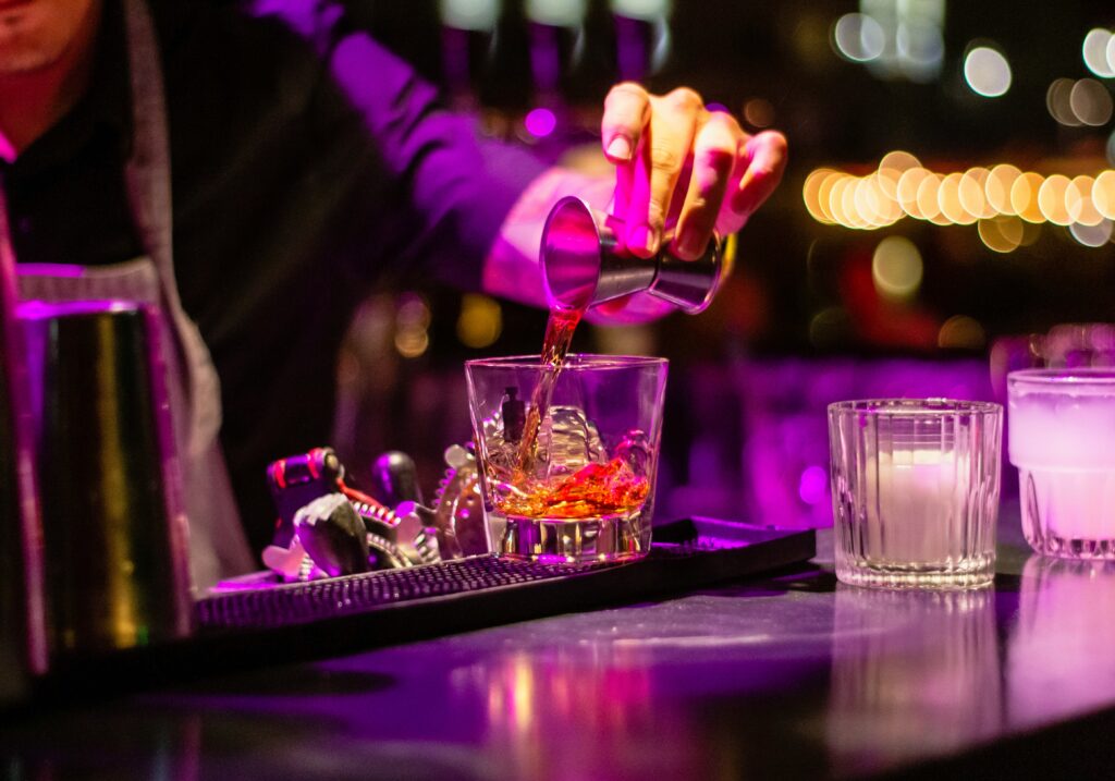 A bartender pours a cocktail in the low pink light of a hidden bar, the kind of room Montreal speakeasies are known for